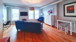 A modern living room with a blue sofa, wooden flooring, a white desk, and a TV on the wall. - Medical District Gem III (Chicago)