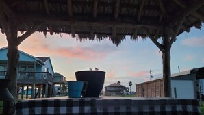 Ein Tisch unter einem Reetdach mit karierter Tischdecke, einem großen schwarzen Topf und einem blauen Eimer.