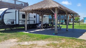 Ein Campingplatz mit überdachtem Picknickbereich, einem Wohnwagen und einem eingezäunten Pool-Bereich.