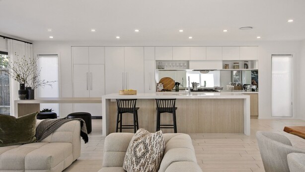 Une cuisine moderne avec des meubles blancs, un îlot central doté de tabourets de bar et un coin repas comprenant un canapé et une table basse.