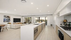 Une cuisine moderne dotée d’un îlot central, un coin repas avec un canapé et un salon avec une télévision et des œuvres d’art.