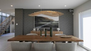 Un espace de salle à manger moderne avec une table en bois, des chaises à revêtement gris, un grand tableau abstrait et un luminaire suspendu original en fibres tressées.