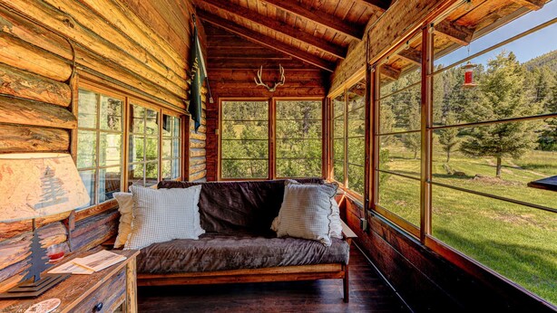 L’intérieur d’une cabane en rondins, avec un banc en bois, une porte en verre et une vue sur une forêt.