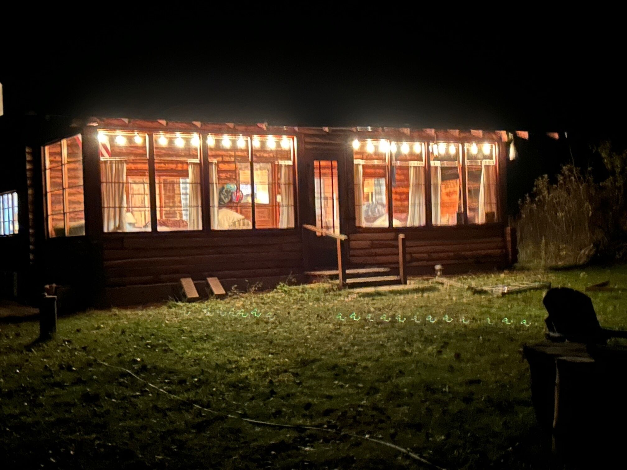 A wooden cabin with multiple windows, a porch, and a grassy yard.