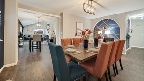 A dining area with a wooden table set for six, surrounded by upholstered chairs. There is a chandelier above the table, and the room has a modern design with a large window and an arched wall. - Sacramento Retreat w/ Pool, Tub, & Backyard Golf Oasis (Sacramento)