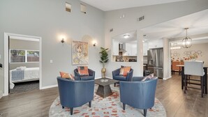 A modern living room with two blue armchairs, a round coffee table, and a large rug. There is a dining area with a table and chairs, and a kitchen with stainless steel appliances. - Sacramento Retreat w/ Pool, Tub, & Backyard Golf Oasis (Sacramento)