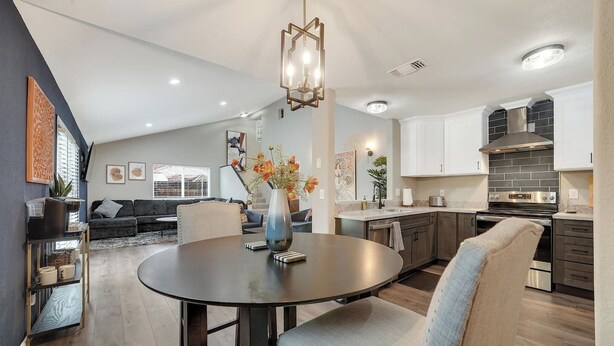 A modern kitchen with dark cabinets, a stainless steel range hood, and a dining area with a round table and chairs. - Sacramento Retreat w/ Pool, Tub, & Backyard Golf Oasis (Sacramento)