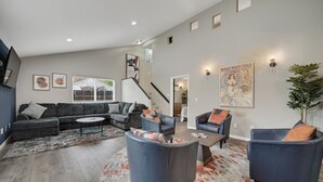 A spacious living room with a grey sectional sofa, two blue armchairs, a coffee table, and a patterned rug. A staircase is visible in the background, leading to another level. - Sacramento Retreat w/ Pool, Tub, & Backyard Golf Oasis (Sacramento)