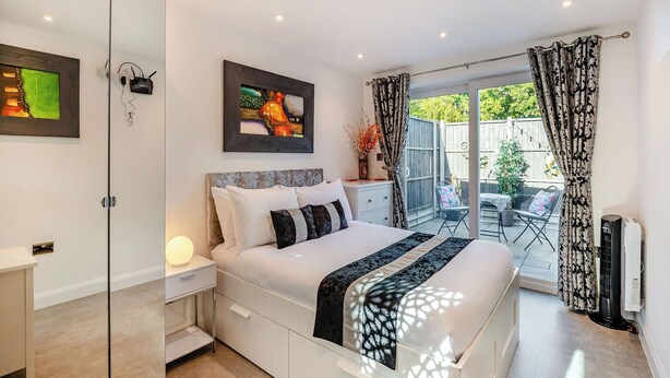 Un dormitorio moderno con una cama grande, un armario de vidrio, una mesita de noche con lámpara, un cuadro en la pared y vistas al patio exterior.