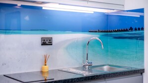 Una cocina moderna con salpicadero de vidrio, un lavamanos de acero inoxidable y un candelabro amarillo.