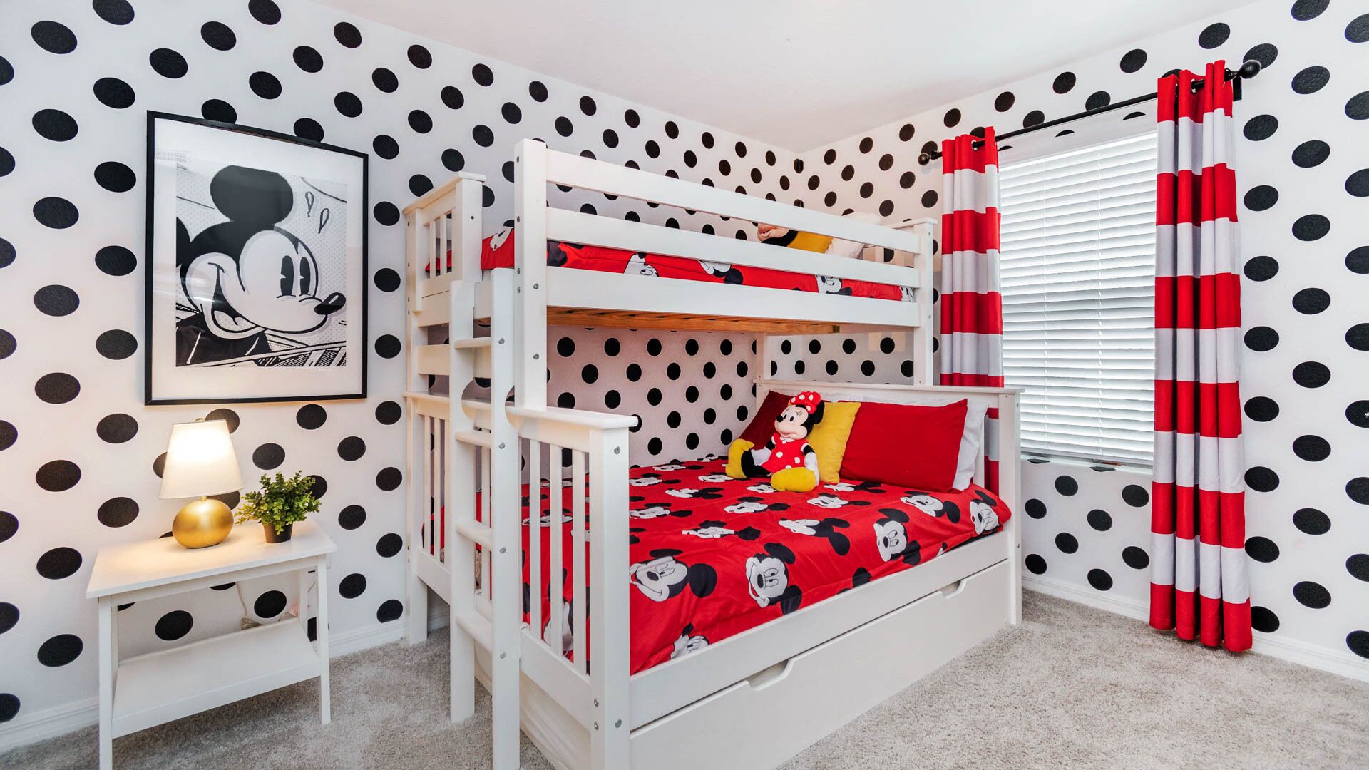 A child’s room with bunk beds, a Mickey Mouse themed bedspread, polka dot wallpaper, and a framed picture on the wall.