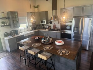 A modern kitchen with stainless steel appliances, wooden bar stools, and pendant lighting.