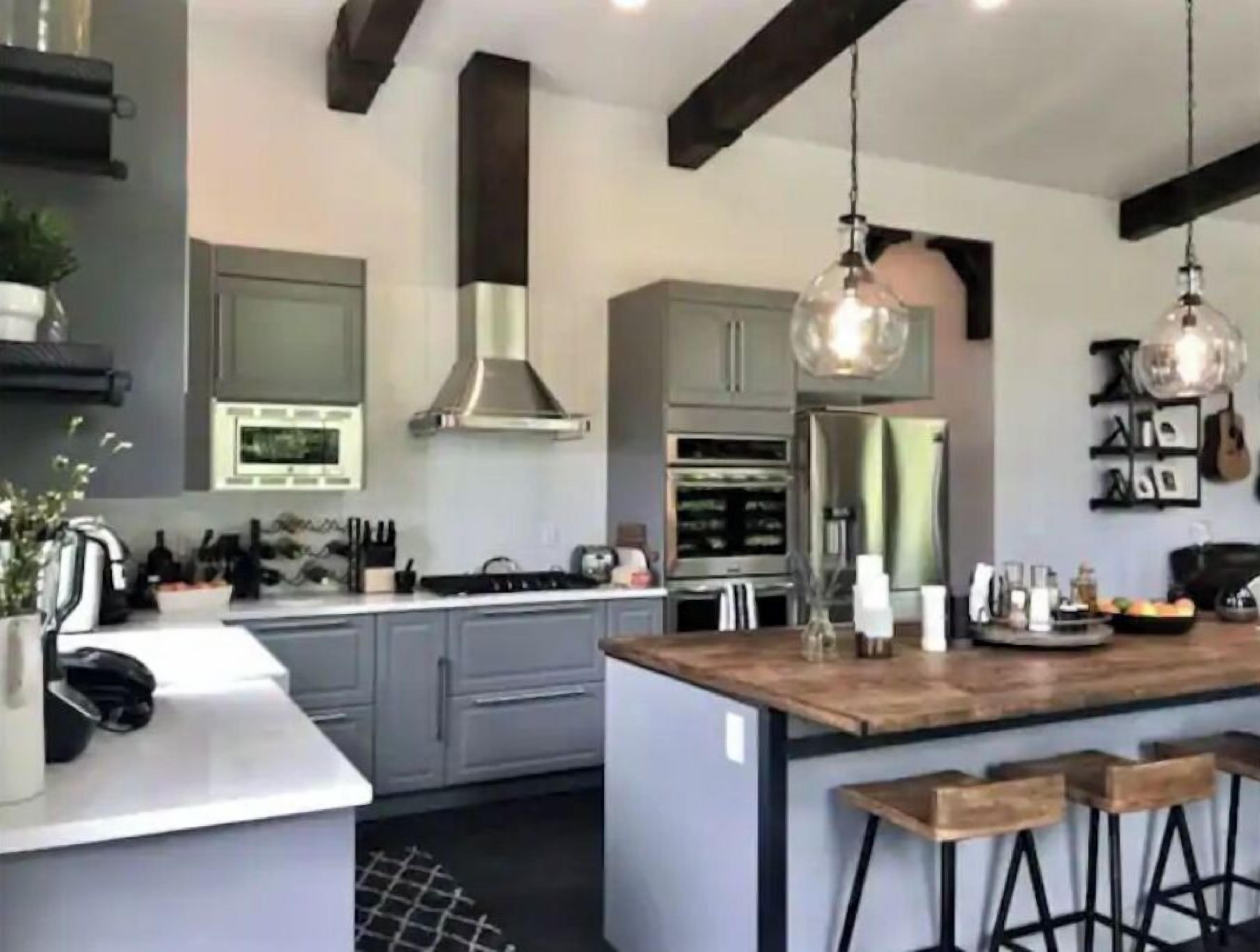Une cuisine moderne avec des meubles gris, des appareils en acier inoxydable et un îlot central en bois doté de tabourets de bar.