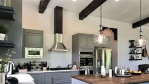 Une cuisine moderne avec des meubles gris, des appareils en acier inoxydable et un îlot central en bois doté de tabourets de bar.