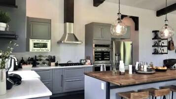 Une cuisine moderne avec des meubles gris, des appareils en acier inoxydable et un îlot central en bois doté de tabourets de bar.