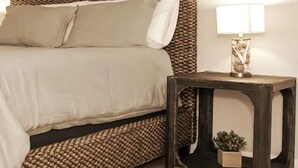 Una cama con cabecera estampada, una mesita de noche con una lámpara y una planta pequeña sobre la mesa.