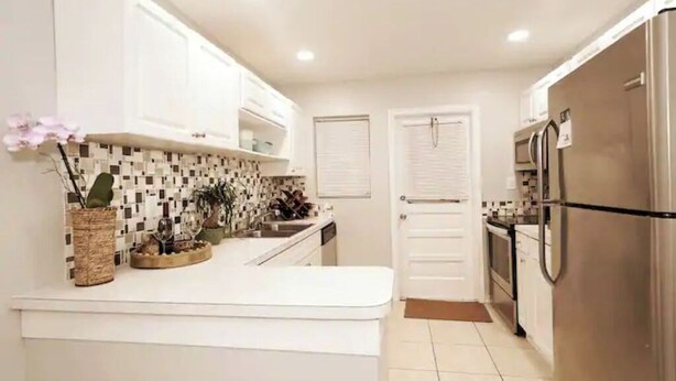 Una cocina moderna con gabinetes blancos, salpicadero de azulejos y refrigerador de acero inoxidable.