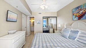 Une chambre avec un grand lit, une commode, un ventilateur de plafond, une télévision et un tableau.