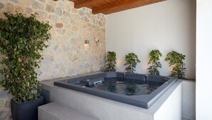 A spa area with a stone wall, a hot tub, and potted plants. - Villa Angeliki - Private villa with pool in Santorini (Thera)