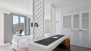 A modern bedroom with a bed, a desk, and a view of a mountain. - Villa Angeliki - Private villa with pool in Santorini (Thera)