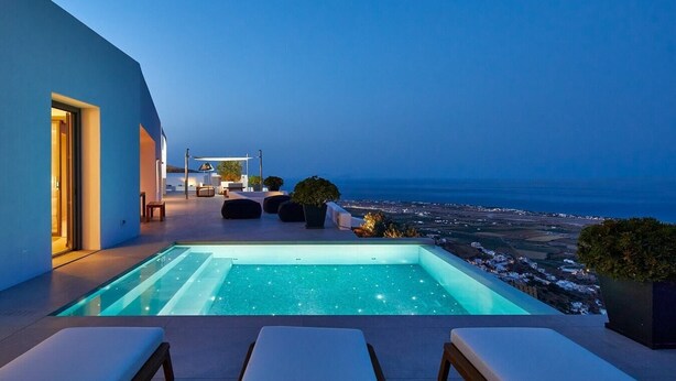 A modern outdoor pool area with a view of the sea, lounge chairs, and a seating area with a table and chairs. - Villa Angeliki - Private villa with pool in Santorini (Thera)
