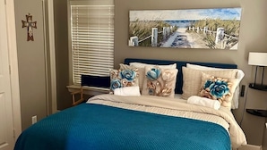 Een slaapkamer met een bed, een raam met zonwering, een schilderij aan de muur en een kruisbeeld aan de muur.