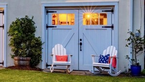 A house with a white exterior, a front door with glass panels, two rocking chairs with cushions, and a small window with shutters. - Gorgeous Carriage House close to USNA, walk to stadium, free parking,  pets+kids (Annapolis)