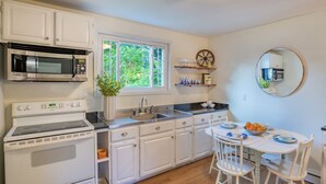 A kitchen with white cabinets, a stove, a microwave, a sink, and a dining area with a table and chairs. - Gorgeous Carriage House close to USNA, walk to stadium, free parking,  pets+kids (Annapolis)