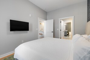 Quarto de hotel com uma cama grande, televisão de tela plana na parede e porta aberta para um banheiro.