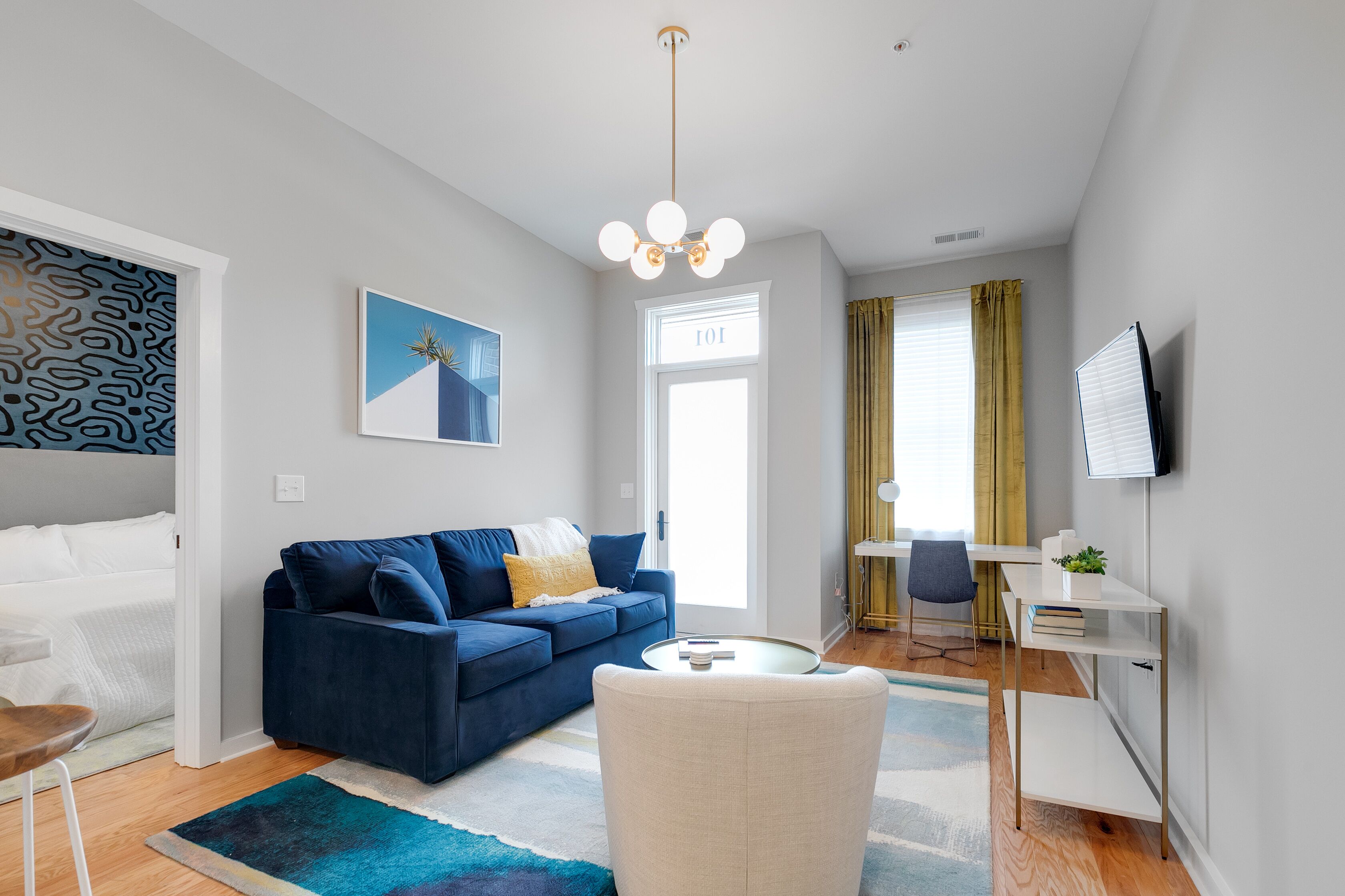A modern living room with a blue sofa, a white armchair, a round coffee table, and a desk with a computer.
