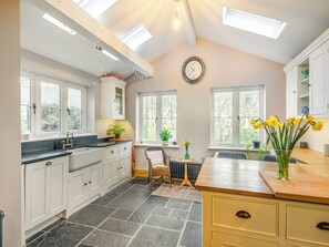 A kitchen with white cabinets, a clock, and a vase of yellow flowers.