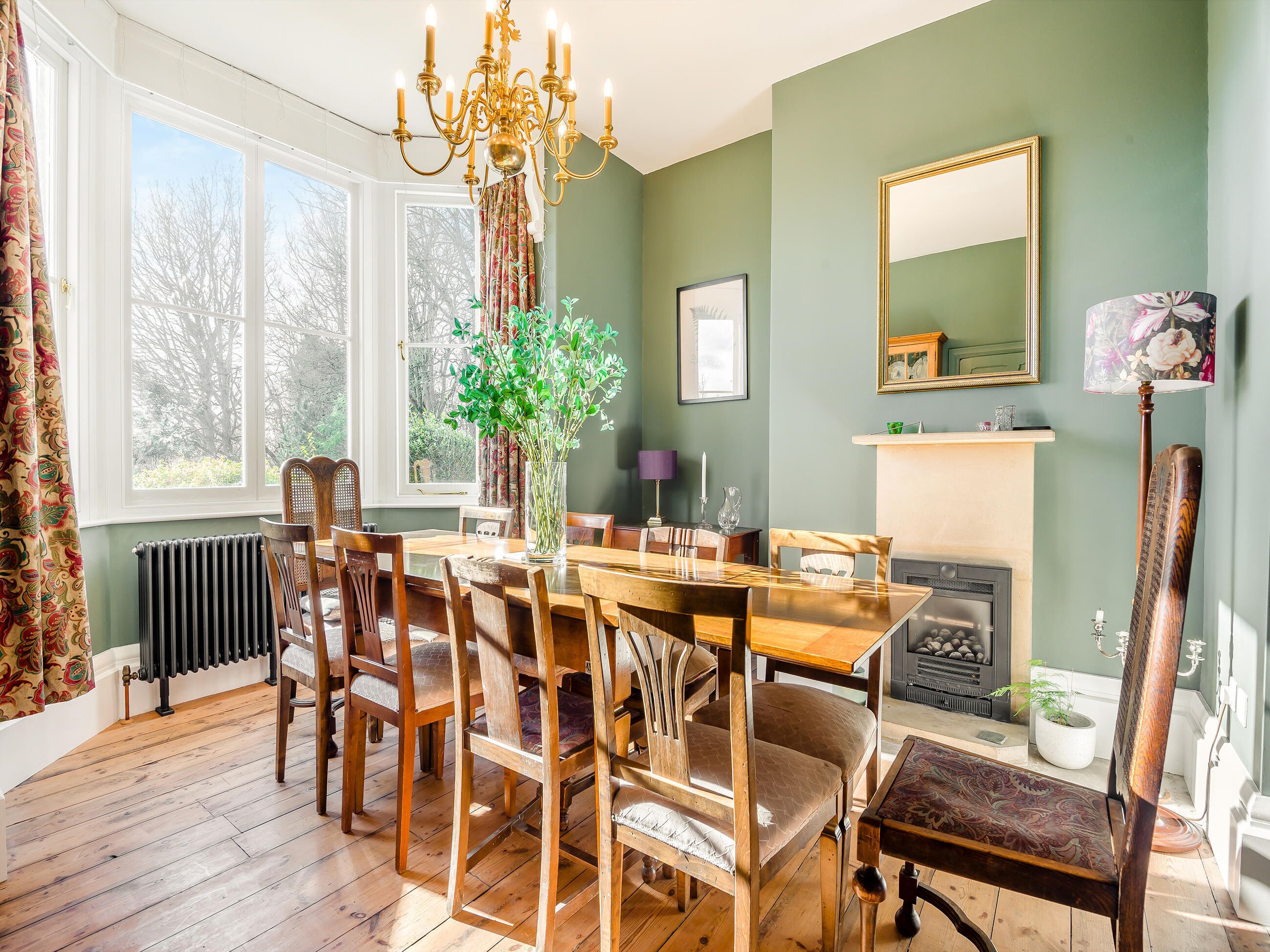 A dining room with a wooden table, chairs, a chandelier, a fireplace, and a large window.