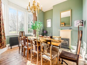 A dining room with a wooden table, chairs, a chandelier, a fireplace, and a large window.