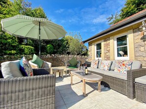 An outdoor patio with wicker furniture, a stone wall, and a building with windows.