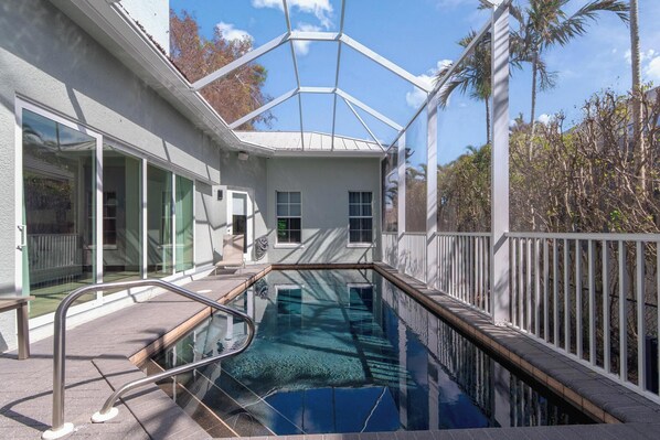 A swimming pool with a glass enclosure, a white building with large windows, and a white fence.