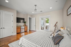 A bedroom with a large bed, a ceiling fan, and a view of the balcony.