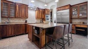 Una cocina moderna con armarios de madera, una isla central con taburetes de bar, electrodomésticos de acero inoxidable e iluminación colgante.