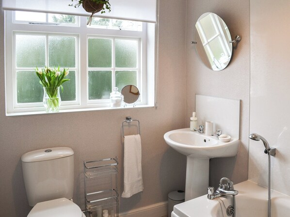 A bathroom with a toilet, sink, and bathtub. There is a window with a plant on the windowsill and a towel rack. - A lovely cottage with a view of the magnificent St James Church Spire. (Louth)