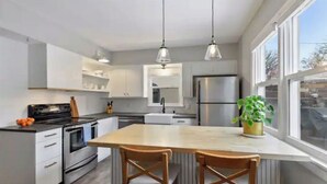 Una cocina moderna con armarios blancos, electrodomésticos de acero inoxidable y un ventanal que proporciona luz natural.