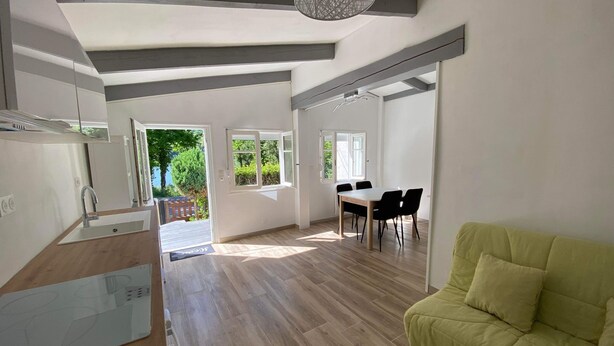 A spacious living area with a dining table and chairs, a sofa, and a kitchen area with a sink and cabinets.
