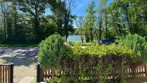 A view of a lake with a car parked near a wooden fence, surrounded by lush greenery.