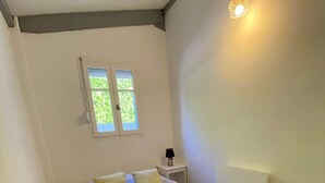 A bedroom with a bed, two windows, a bedside table with a lamp, and a wall-mounted light fixture.