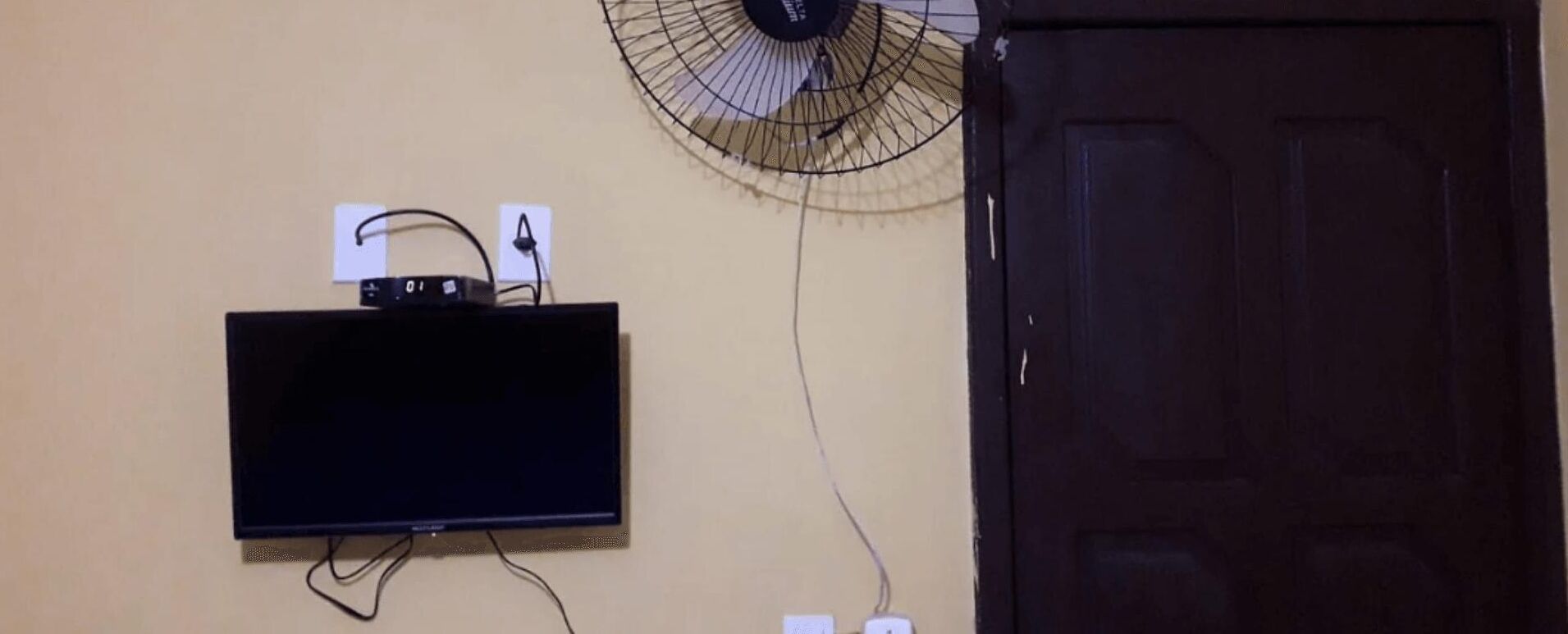 Un téléviseur fixé au mur, avec une multiprise et un ventilateur mural.