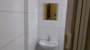 A small bathroom with white tiles, a sink, and a mirror. - Sana Aluguel Economico (Macaé)