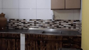 A small kitchen with a tiled backsplash, a sink, and wooden cabinets. - Sana Aluguel Economico (Macaé)