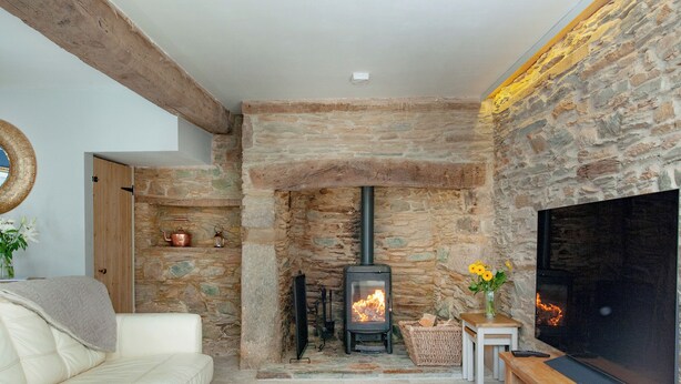 Una sala de estar acogedora con chimenea de piedra, un sofá blanco y un televisor de pantalla plana.