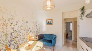 A room with a blue sofa, a round table with a basket, a hanging light fixture, and a floral wallpaper.