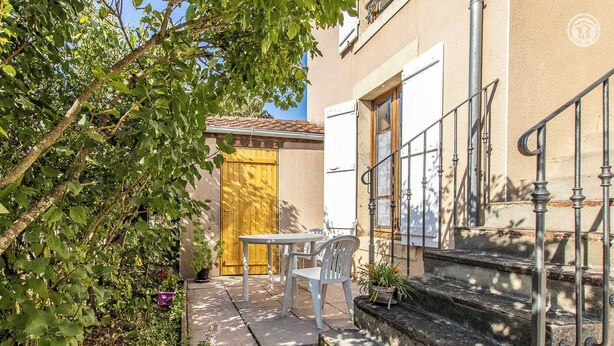 A courtyard with a table and chairs, a wooden door, and a staircase leading to a building.