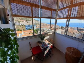 A balcony with a view of a coastal cityscape, a table with a colorful tablecloth, and a wicker basket.