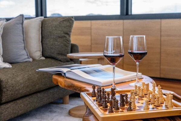 Un salon chaleureux avec un jeu d’échecs, deux verres de vin rouge et un livre posé sur une table en bois.